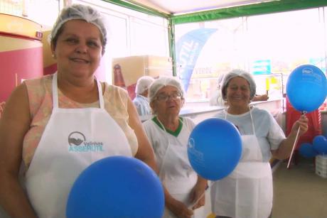 #PraCegoVer: Mulheres usam avental e touca de papel segurando balões azuis. Imagem feita na Festa do Figo 2019.