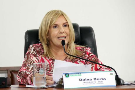 #PraCegoVer: Foto mostra a presidente da Câmara, vereadora Dalva Berto, sentada em seu lugar, segurando um documento e discursando para o público.