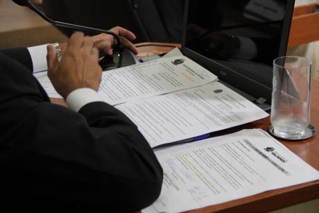#PraCegoVer: Foto mostra a mão de um vereador em cima da bancada, com documentos.