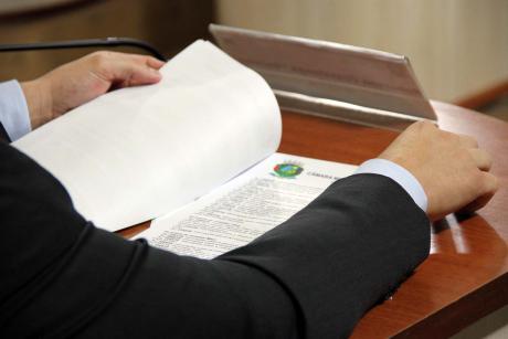 #PraCegover: Foto mostra mão de vereador folheando um documento.