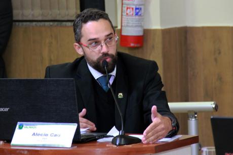 #PraCegoVer: Foto mostra o vereador Alécio Cau sentado em seu lugar no plenário, dirigindo a palavra à Mesa Diretora.