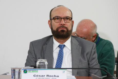 #PraCegoVer: Vereador César Rocha, sentado na mesa diretora, olha para a frente em direção ao plenário da Câmara