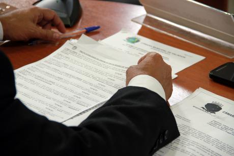 #PraCegoVer: Foto mostra os braços de um vereador sobre alguns documentos, durante a sessão da Câmara. Nas mãos, ele segura uma caneta.
