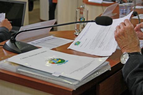 #PraCegoVer: Foto mostra mão de vereador folheando documentos na mesa, durante a sessão ordinária.