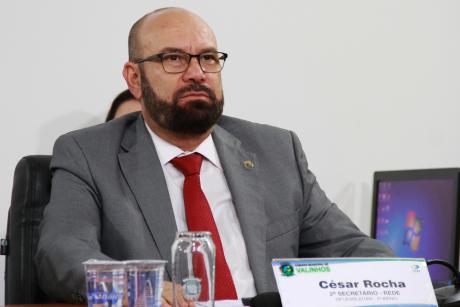 #PraCegoVer: Vereador César Rocha olha para a frente enquanto acompanha a sessão, sentado em seu lugar na mesa diretora