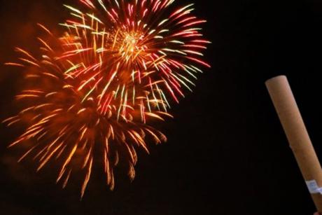 #PraCegoVer: Foto mostra fogos de artifício colorindo o céu durante a noite. No canto direito há um tubo para lançamento dos fogos.