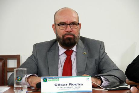 #PraCegoVer: Vereador César Roca acompanha a sessão sentado em seu lugar na Mesa Diretora. Em sua frente, há uma placa com seu nome.