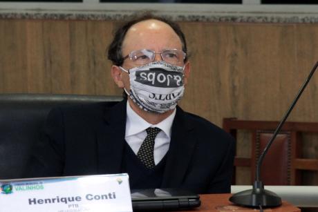#PraCegoVer: Vereador Henrique Conti acompanha sessão de sua tribuna na Câmara. Ele usa uma máscara com estampa de recortes de jornal.  