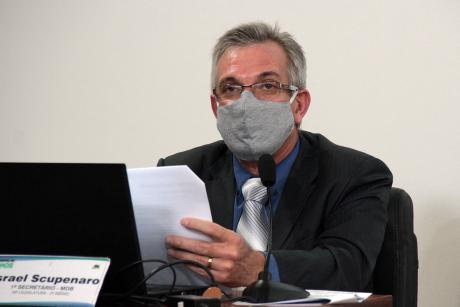 #PraCegoVer: Vereador Scupenaro olha à frente enquanto discursa e segura um papel em sua tribuna na Câmara. Ele usa uma máscara cinza. 