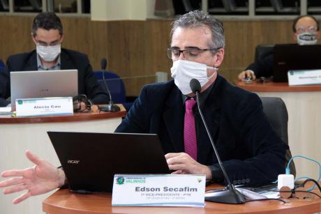 #PraCegoVer: Vereador Secafim fala e gesticula de sua tribuna. Ele usa uma máscara branca e lê algo em seu computador portátil. 
