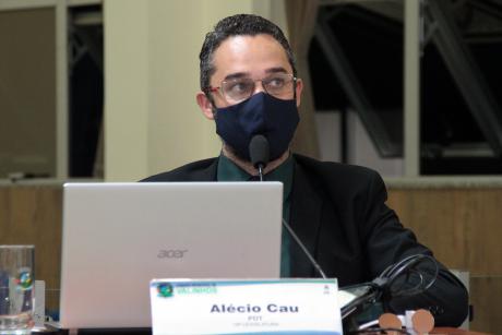#PraCegoVer: Vereador Alécio Cau acompanha a sessão sentado à sua tribuna. Ele tem um computador portátil aberto diante de si e usa uma máscara. 