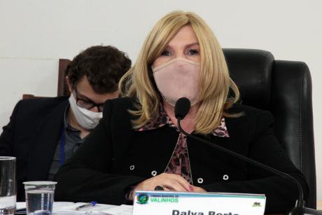 #PraCegoVer: Vereadora Dalva Berto fala ao microfone sentada à sua tribuna na mesa diretora. Ela usa uma máscara.