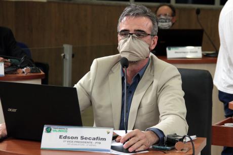 #PraCegoVer: Vereador Edson Secafim fala ao microfone sentado à sua tribuna durante a sessão. Ele usa uma máscara e tem um computador portátil aberto diante de si. 