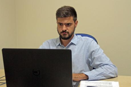 #PraCegoVer: Vereador Gabriel Bueno acompanha a sessão em um computador portátil em uma mesa. Na mesa há papeis. 