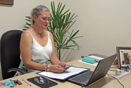 #PraCegoVer: Vereadora Simone Bellini acompanha a sessão de 09/03/2021 com o auxílio de um celular e um computador portátil. Ela senta-se à sua mesa. 