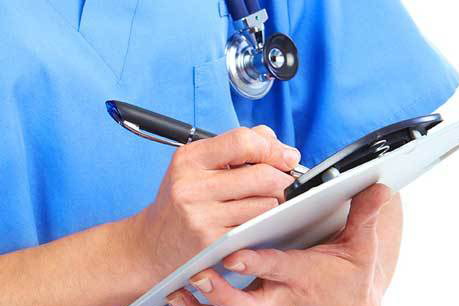 #PraCegoVer: Foto mostra profissional da saúde vestido com traje azul, portando um estetoscópio e com prancheta e caneta em mãos. 