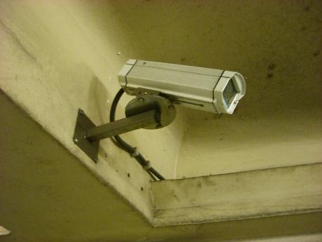 #PraCegoVer: Foto mostra câmera de segurança presa a viga de concreto em algum edifício. 