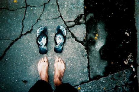 #PraCegoVer: Foto mostra pés de pessoa de rua, em frente a uma sandália de dedo de borracha. 