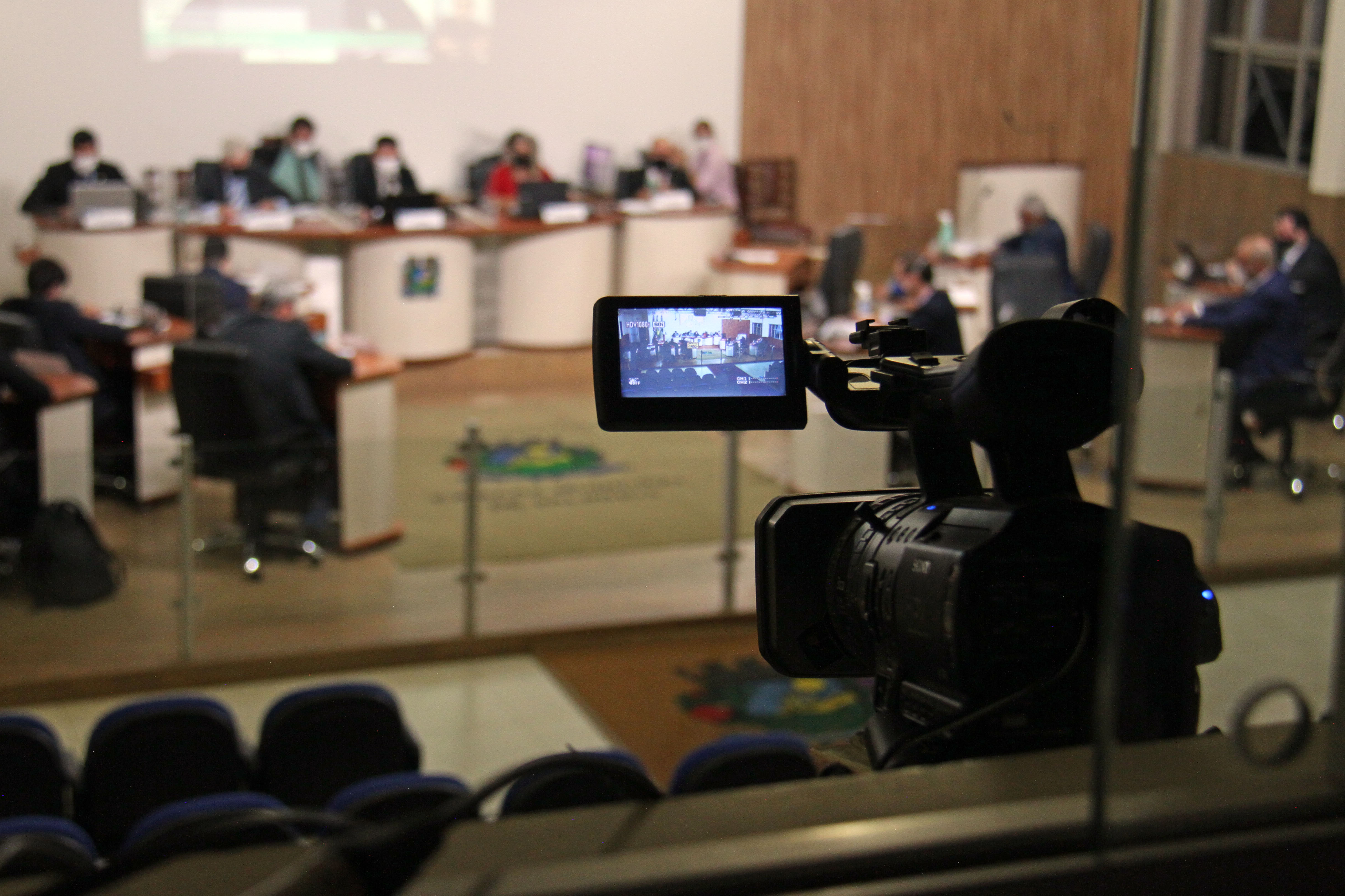 #PraCegoVer: Foto mostra detalhe do display de gravação da câmera filmadora da TV Câmara. Ao fundo estão os vereadores no plenário.