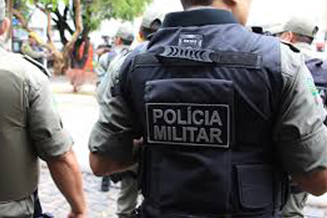 #PraCegoVer: Foto mostra policial militar de costas em uma ação. Atrás, no colete, está escrito Polícia Militar.