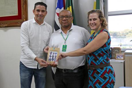 #PraCegoVer: Franklin, Luiz Silva e Ana Paula Galante para foto em frente a bandeiras segurando o livro "Educação Antirracista". 