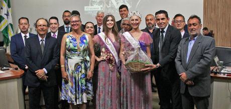 #PraCegoVer: Usando vestidos, faixas e coroas, rainha e princesa da Festa do Figo posam para foto com vereadores