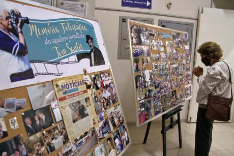 #PraCegoVer: foto mostra dois painéis com fotos tiradas pelo jornalista Tom Santos. Uma visitante presente na exposição aprecia o material.