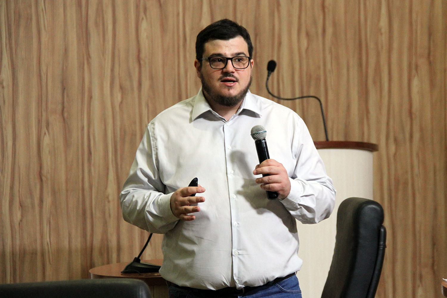 #PraCegoVer: foto mostra o professor Alexandre Siloto Assine segurando um microfone, ministrando o curso para o público.