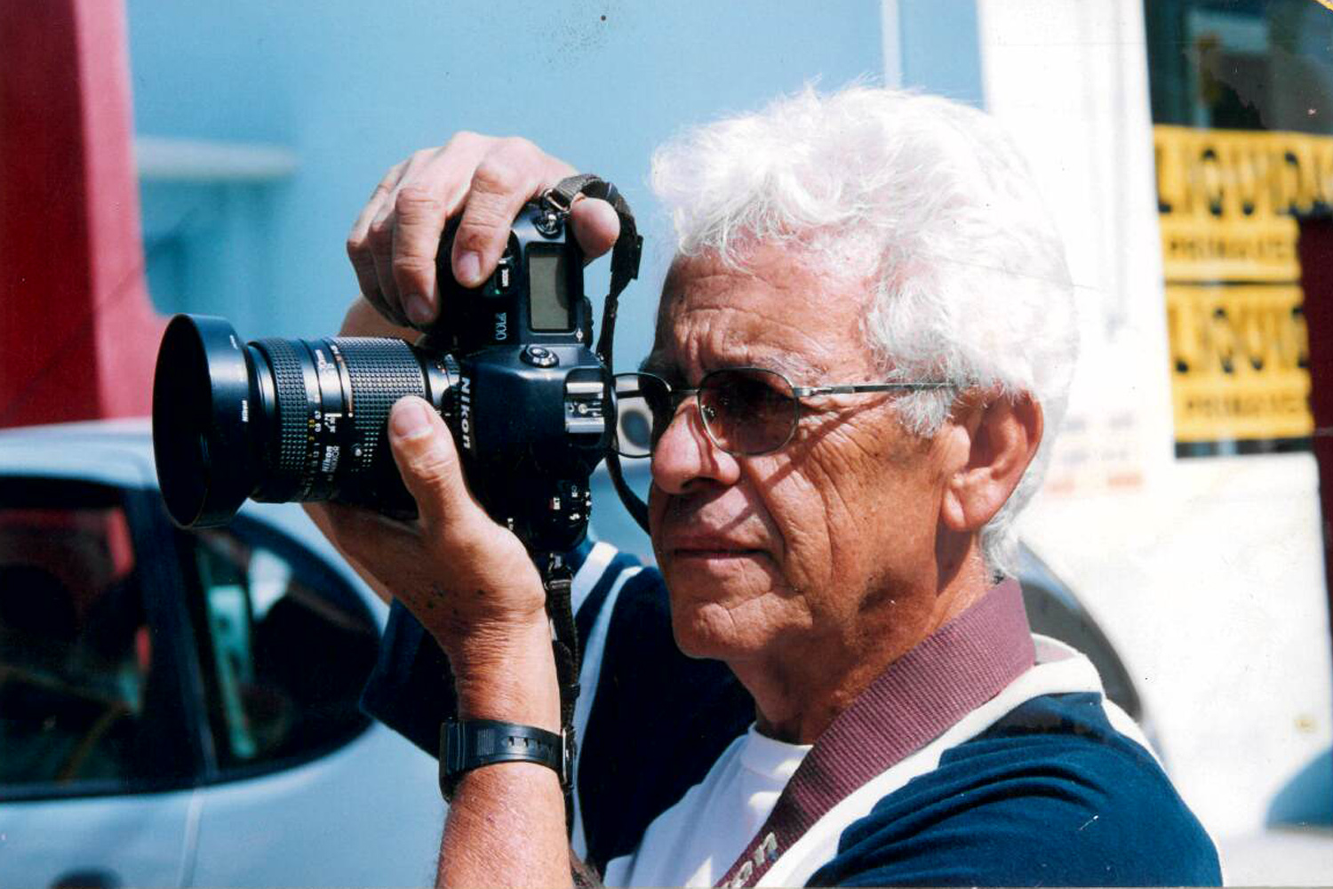 #PraCegoVer: foto mostra o jornalista Tom Santos com sua máquina fotográfica, registrando uma cena urbana.